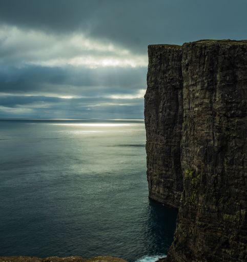 A beautiful scenery of rocky cliffs by the sea in the Faroe Islands under a cloudy sky