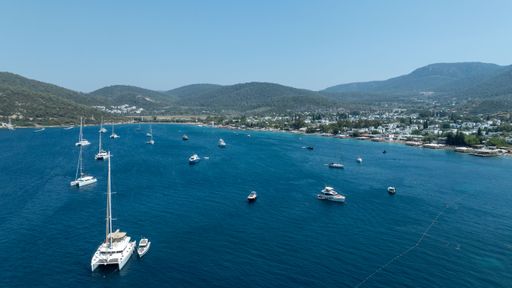 Aerial view of a serene bay with yachts and sailboats in Bodrum, Turkey, surrounded by lush hills under a clear blue sky.