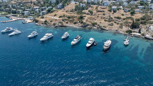 Aerial view of luxury yachts anchored in a serene bay with turquoise waters and hillside villas in Bodrum, Turkey.