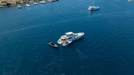 Aerial view of luxury yachts anchored in a serene blue sea, with a scenic coastline in the background.