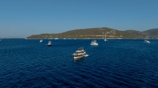 Boats sailing on a clear blue sea with a scenic island backdrop under a bright sky.