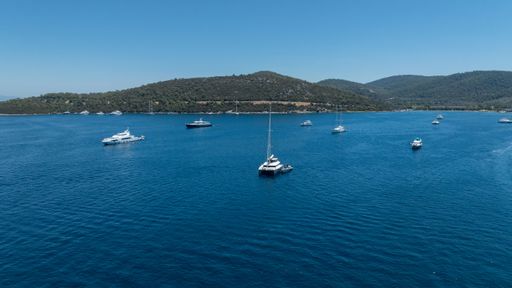 A serene view of yachts floating on a clear blue sea with lush green hills in the background under a bright sky.