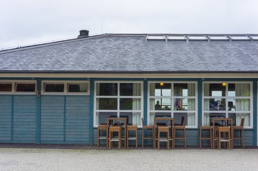 A shot of wooden chairs and tables in front of a small blue cafe building at the beach in Gdynia, Poland