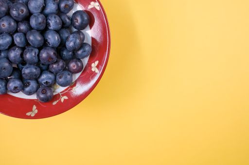view of sweet tasty blueberries on a plate on a yellow background with text space