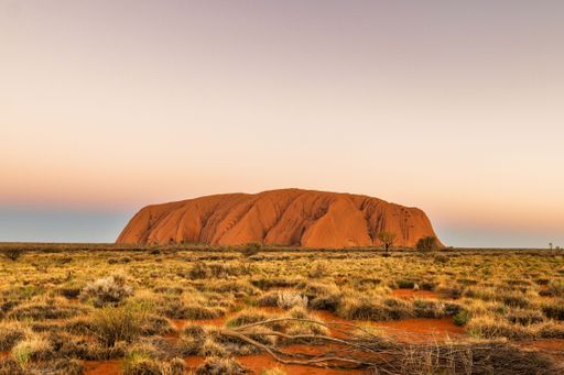 A stunning view of Uluru at sunset with a clear sky in Australia's outback, showcasing the iconic rock formation and surrounding landscape.