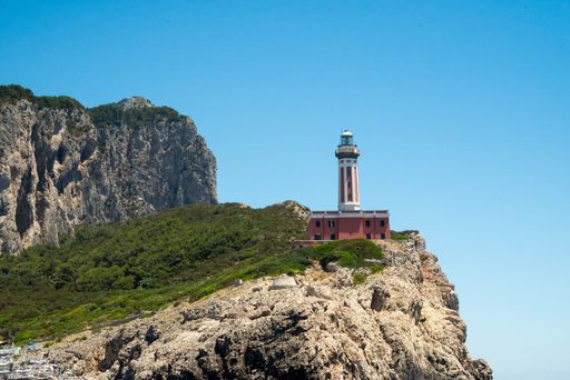 A picturesque lighthouse perched on a rocky cliff with lush greenery and a clear blue sky, capturing the essence of coastal beauty.