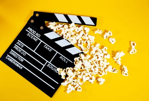 A film clapperboard with scattered popcorn on a vibrant yellow background, symbolizing cinema and entertainment.