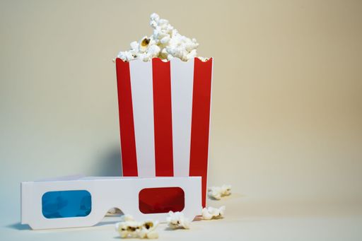 A box of popcorn with 3D glasses on a neutral background, symbolizing a classic movie experience.