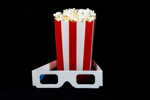 A striped popcorn bucket and 3D glasses on a black background, symbolizing a classic cinema experience.