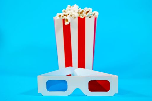 A close-up of 3D glasses and a popcorn box on a vibrant blue background, evoking a cinema experience.