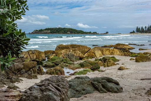 Scenic coastal view with rocky shoreline and distant island under a partly cloudy sky.