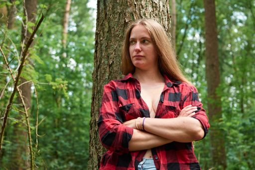 The beautiful blonde girl leaning on the tree with her arms crossed.