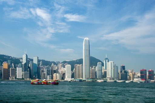 Skyline of Hong Kong with iconic skyscrapers and a colorful ferry on Victoria Harbour under a clear blue sky.