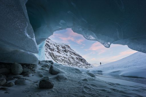 An icy cavern framing a distant snowy mountain peak at twilight, showcasing the serene beauty of a polar landscape.