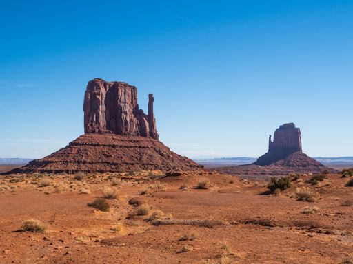 A majestic view of Monument Valley's iconic sandstone buttes under a clear blue sky, showcasing the stunning desert landscape.