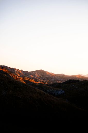 A serene mountain landscape at sunset with warm light casting over the rocky terrain.