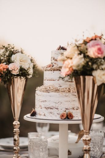 A vertical closeup of a white wedding cake with small bouquets of flowers in golden vases.