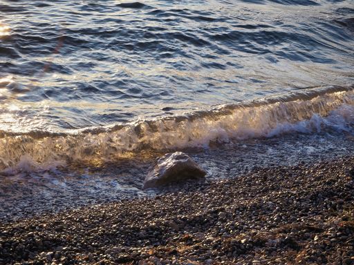 A beautiful view of the sea waves washing in on small pebbles at the shore during sunset