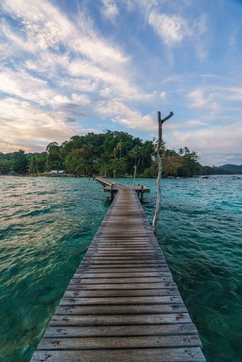 A serene wooden pier extends over turquoise waters towards a lush island under a vibrant sky, capturing tropical tranquility.
