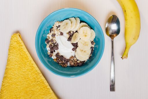 A high angle shot of oatmeal with chocolate chips and bananas in a blue plate with banana and a spoon on the right side