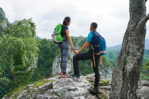 A beautiful shot of a loving couple holding hands and standing on the edge of a cliff looking at the hill outlines on the horizon