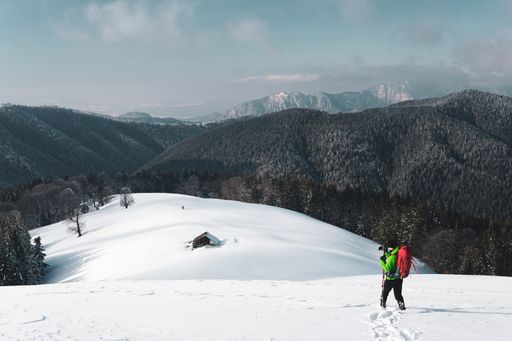 A male hiker taking photos of a winter alpine mountain and a snow covered hut below