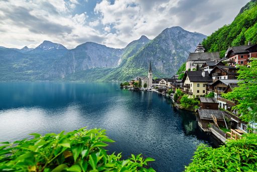 Scenic view of Hallstatt village by the lake with mountains and lush greenery under a partly cloudy sky in Austria.