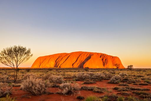 A scenic view of Uluru at sunset with a clear sky, showcasing the iconic red rock formation.
