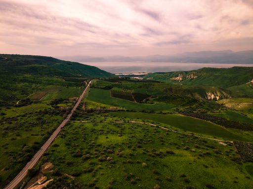 A breathtaking view of the southern Golan Heights with lush green hills and the Sea of Galilee in the background under a cloudy sky.