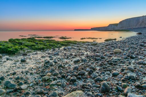 The reflection of a magnificent sunset over the peaceful ocean with rocks covered with moss