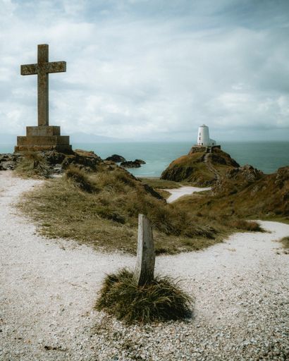 A vertical shot of a Twr Mawr Lighthouse in Wales with the a big statue of cross