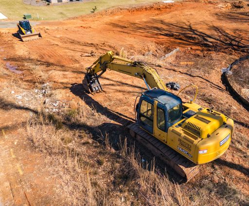 Aerial view of construction site with yellow excavator and bulldozer on red earth, showcasing heavy machinery in action