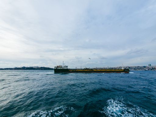 A cargo ship sails through the Bosphorus Strait with a view of Istanbul's skyline under a cloudy sky