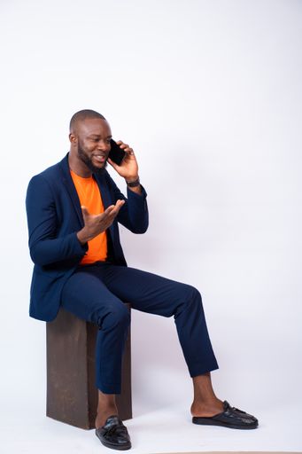 A vertical shot of an African businessman posing with a phone in front of a grey wall