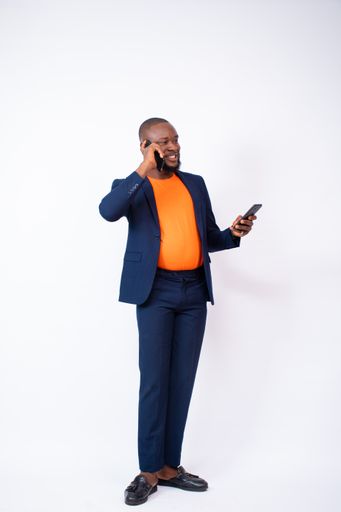 A vertical shot of an African businessman posing with a phone in front of a grey wall