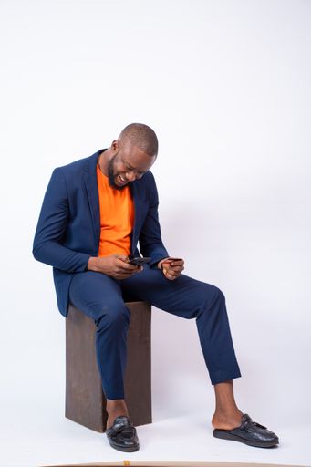 A vertical shot of an African businessman posing with a phone in front of a grey wall