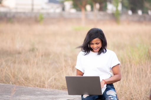 A closeup shot of a young African female posing with her laptop in a field