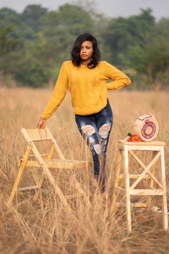 A portrait of a beautiful African female in a yellow sweater in a field