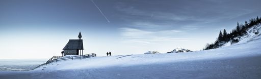 A beautiful panoramic shot of two skiers near a small house in the middle of a snowy forest