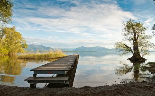 A beautiful shot of a wooden deck leading to the sea with mountains on the background