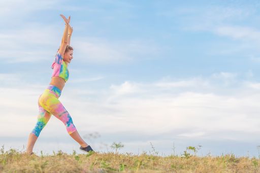 Young woman in a bright tracksuit put her leg forward and raised her arms high up. Preparing to perform a gymnastic exercise. Outdoor sports.
