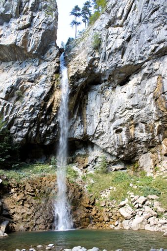 A vertical shot of a beatiful waterfall running down a rocky cliff into a small pond in the wilderness