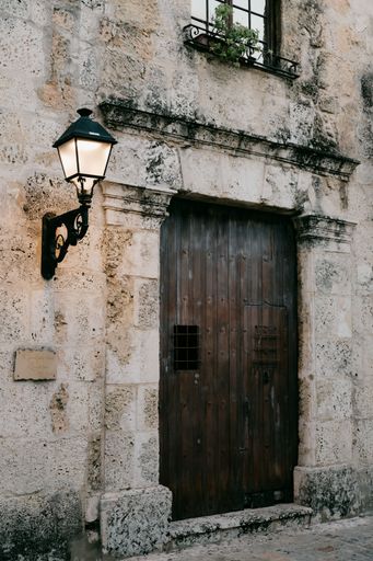 Rustic stone wall with an old wooden door and vintage lamp in a historical European street.