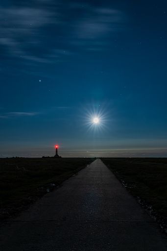 A vertical shot of a pier leading to the sea with a shining star in the sky