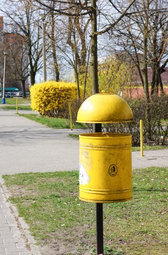A vertical shot of a yellow trash bin on a steel post in a park