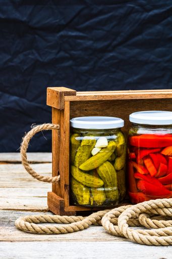 A closeup of glass jars with pickled vegetables - red bell peppers and pickled cucumbers