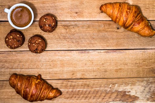 A top view of delicious croissants, chocolate biscuits and a cup of coffee on a wooden table