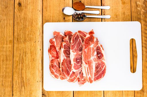 A top view of pork chops with condiments on a white cutting board on a wooden table