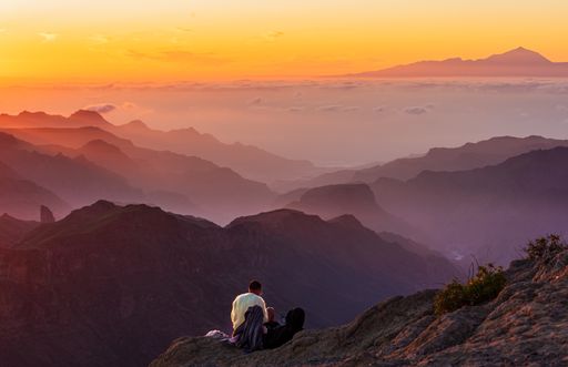 A person sitting on the edge of the mountain with beautiful mountains in the background