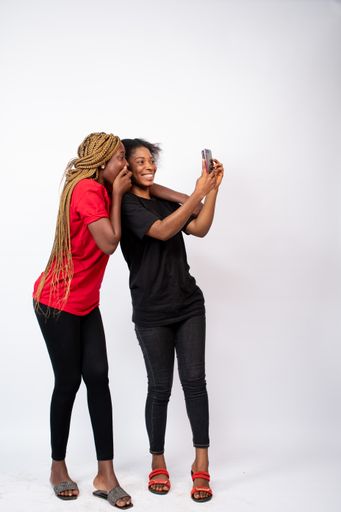 A pair of young African female friends happily taking a selfie isolated on a white background